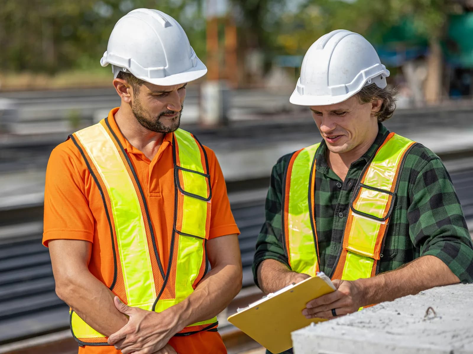 Stefan Brenner und Tobias Kirchner in Helm und Warnweste auf der Baustelle, beim Blick auf das Klemmbrett